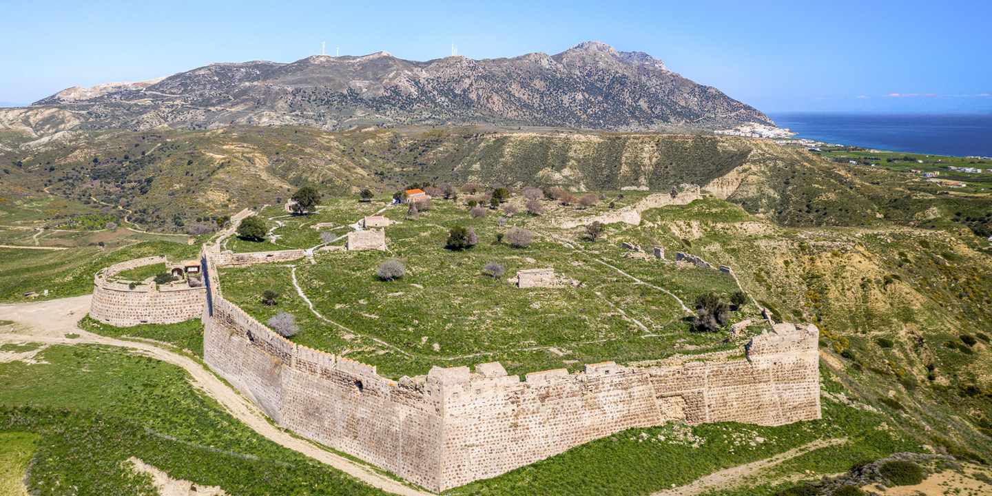 Luftaufnahme der Burg Antimachia auf Kos mit Festungsmauern, Hügellandschaft und Meer im Hintergrund