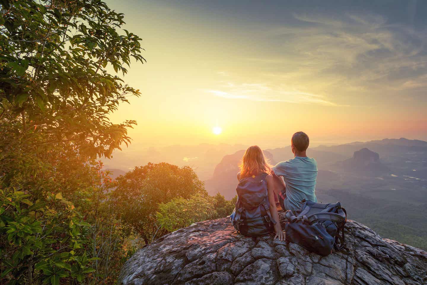 Rhodos Urlaub mit DERTOUR. Paar sitzt auf einem Fels und schaut in den Sonnenuntergang