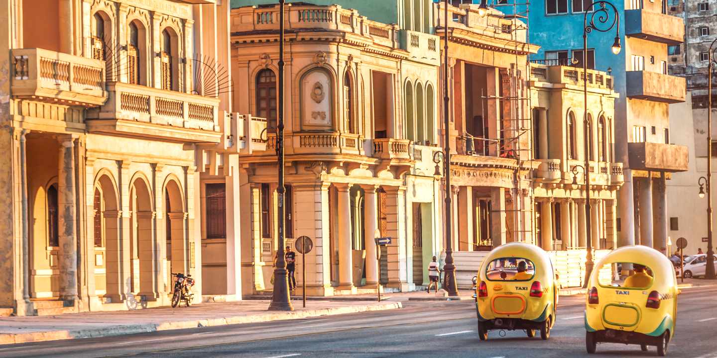 Zwei gelbe, runde Coco-Taxis stehen vor einer historischen Häuserzeile in Havanna