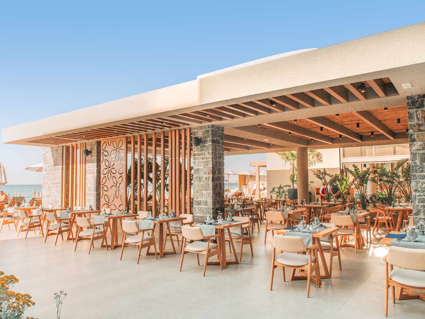 Außenbereich im Sentido Unique Blue Resort auf Kreta mit überdachter Terrasse, Holztischen, Polsterstühlen und Blick zum Meer
