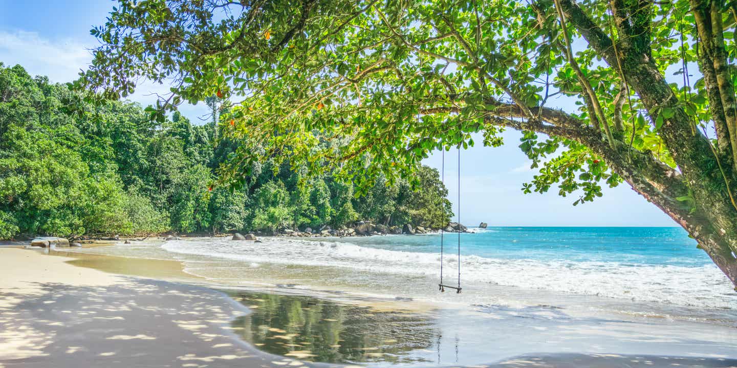 Thailand Urlaub am leeren, seichten Sandstrand, überschattet von einem Baum mit Schaukel