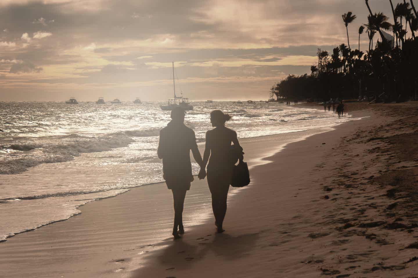 Samana Urlaub mit DERTOUR. Paar spaziert am Strand der Dominikanischen Republik Hand in Hand in der Abendsonne