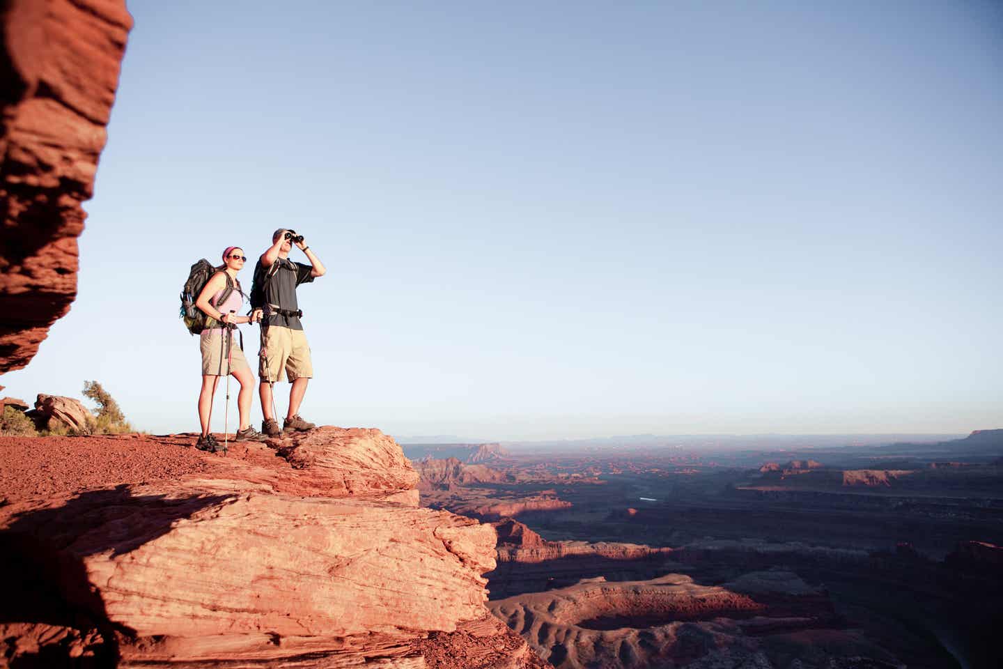 Ein junges Paar steht im Utah-Urlaub auf einem Felsplateau und blickt in die Ferne