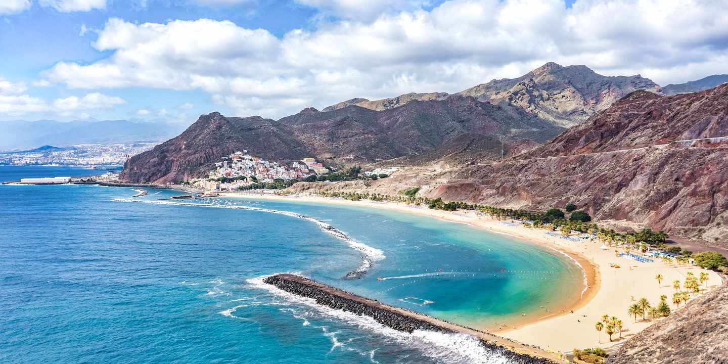 Playa de las Teresitas auf Teneriffa mit hellem Sandstrand, Palmen und ruhigem Wasser vor grünen Bergen
