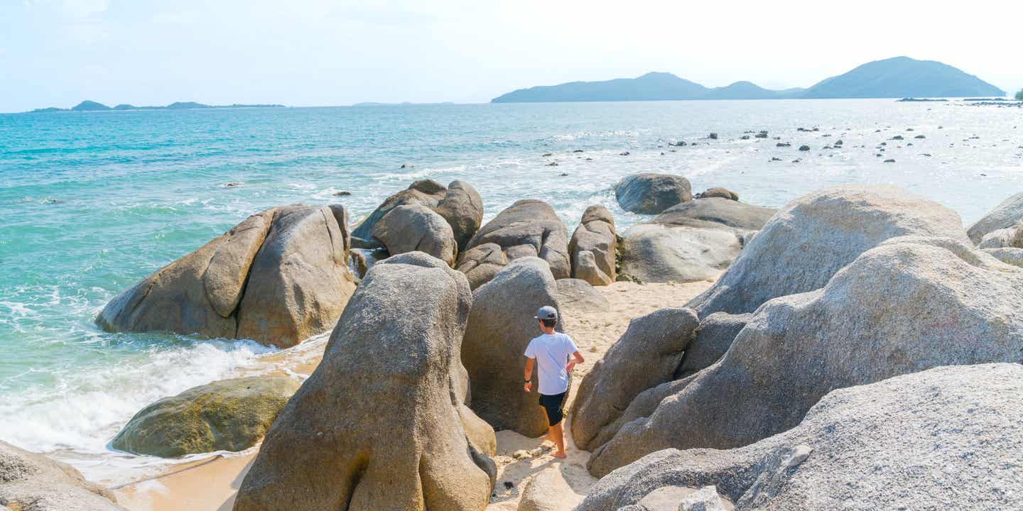 Kind erkundet spielerisch die ikonischen Felsen am Strand der tropischen Insel Ko Samui in Thailand  