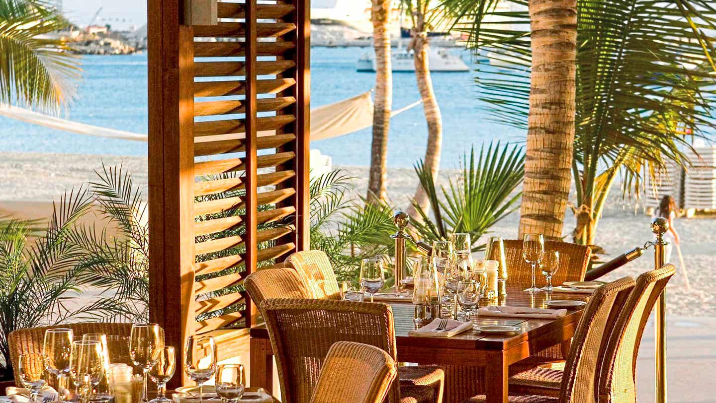 Tische und Stühle aus Holz mit Palmen und Strand im Hintergrund, Restaurant