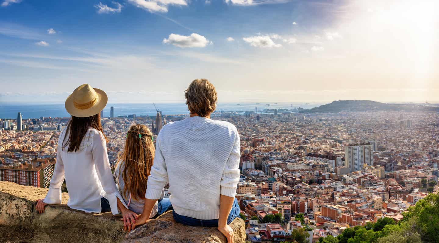 Eltern mit Kind schauen von einem Aussichtspunkt auf die Skyline von Barcelona
