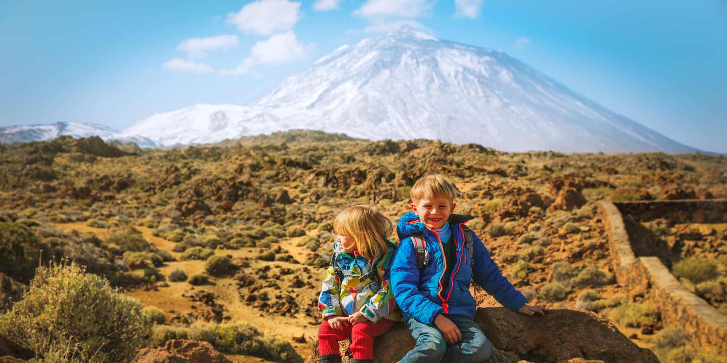 Zwei Kinder im Teide Nationalpark auf Teneriffa, im Hintergrund der schneebedeckte Pico del Teide