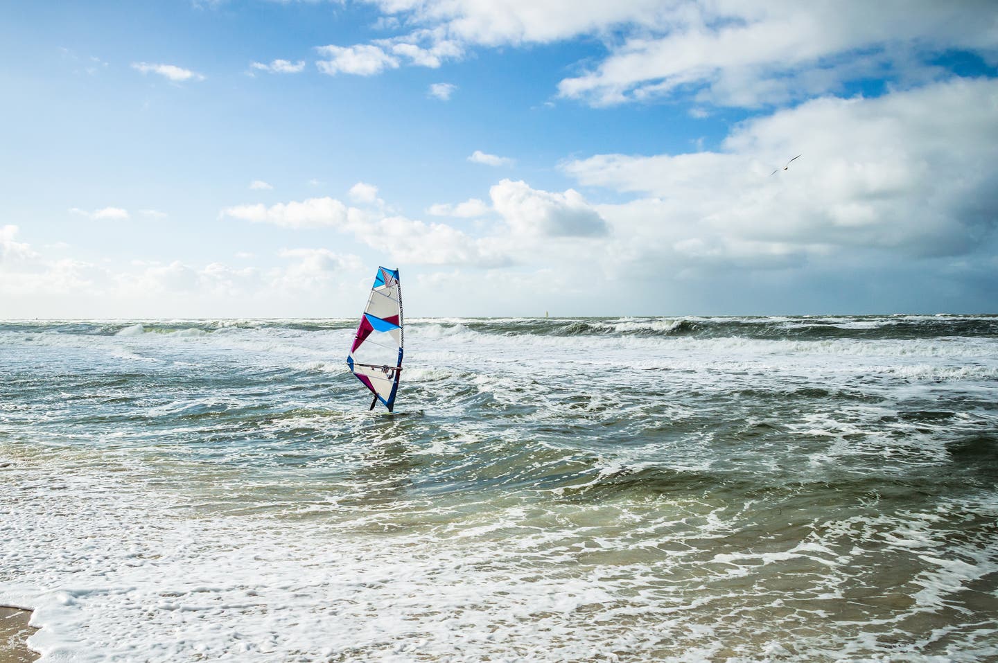 Blick auf Meer, wellenumtost mit einem Surfer auf dem Wasser