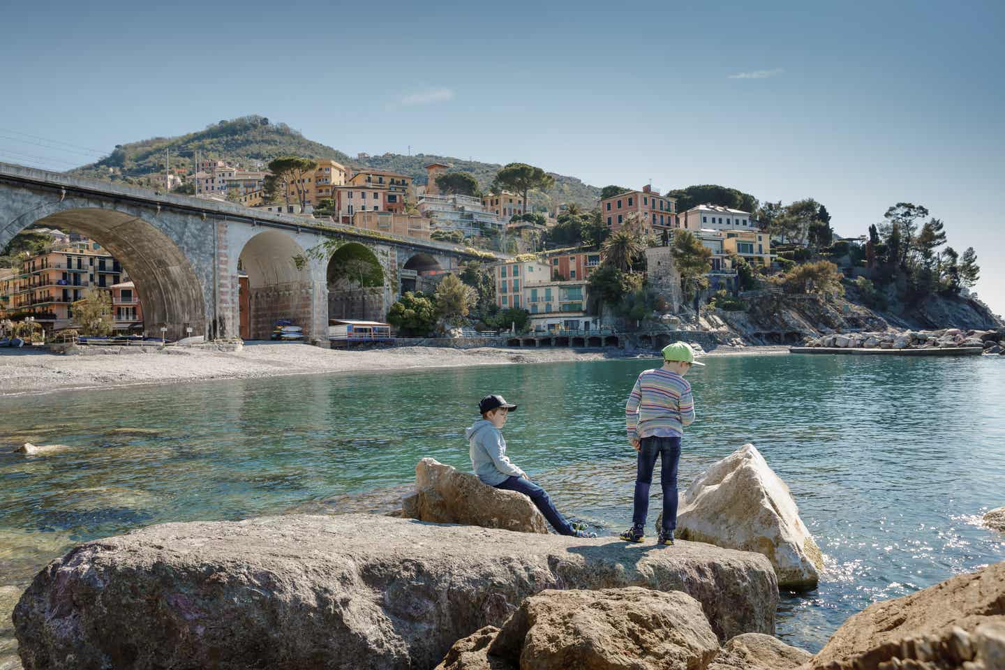 Ligurien Urlaub mit DERTOUR. Zwei Jungen spielen am Mittelmeer. Im Hintergrund der Ort Zoagli in den Cinque Terre