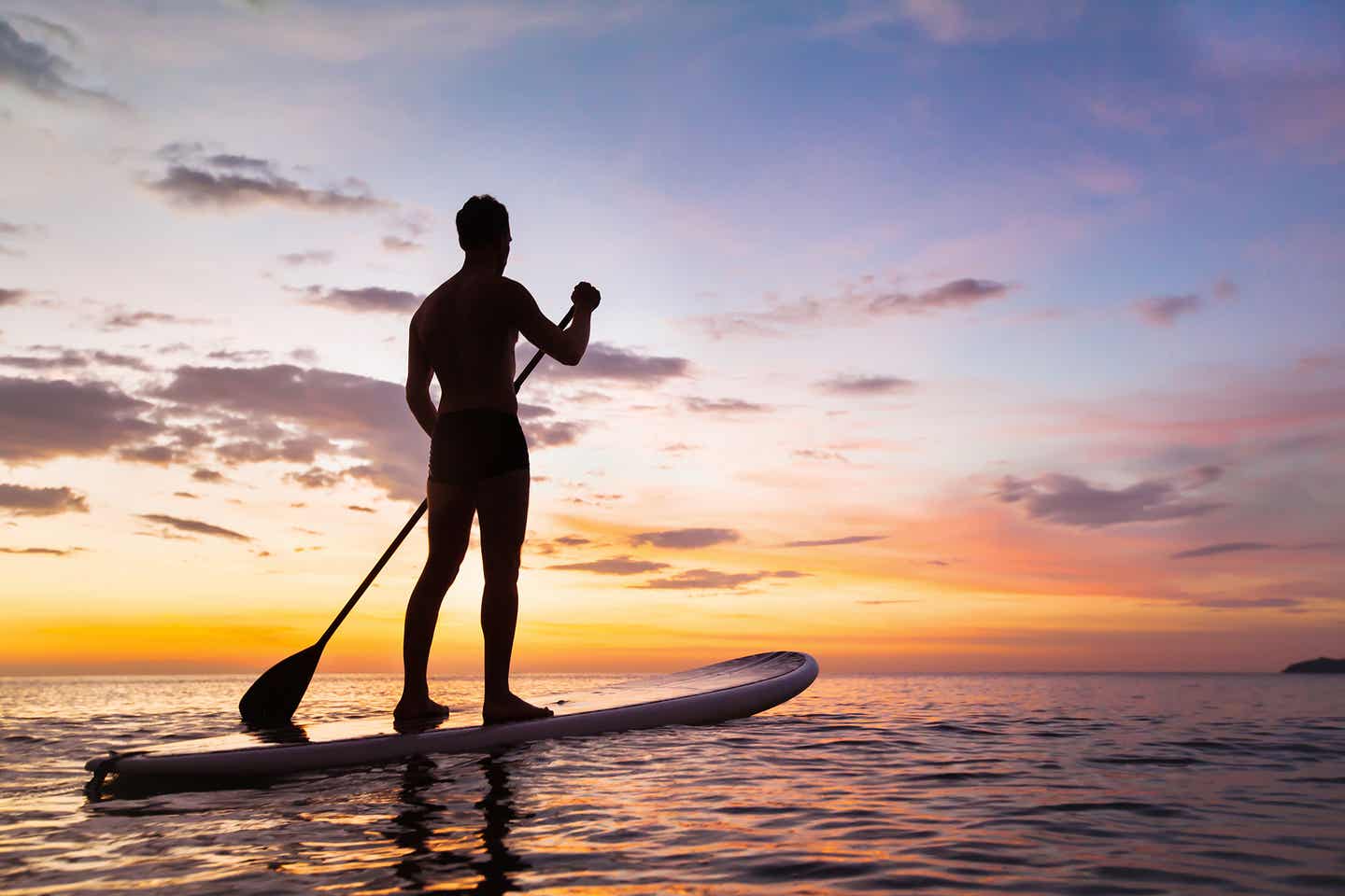 Stand-up-padler auf dem Meer bei Sonnenuntergang