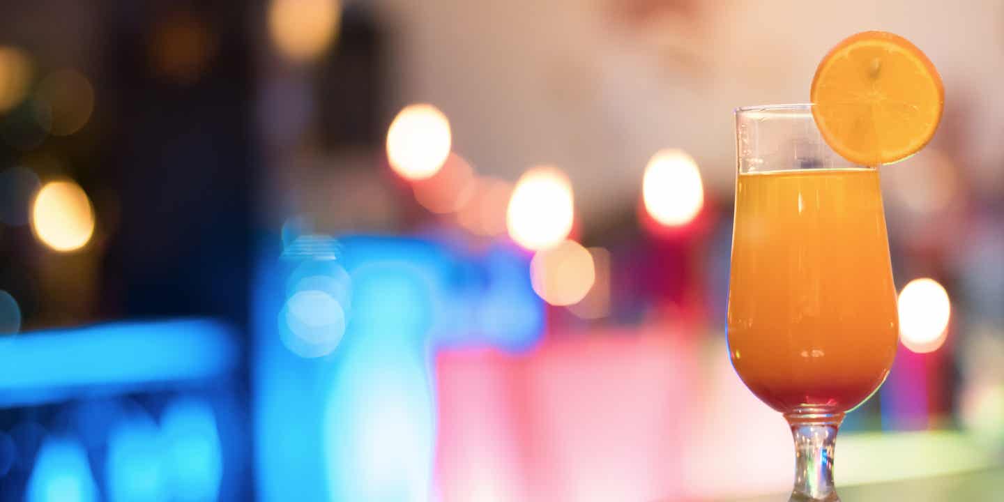Cocktail mit Orangenscheibe bei Festempfang vor bunter Beleuchtung