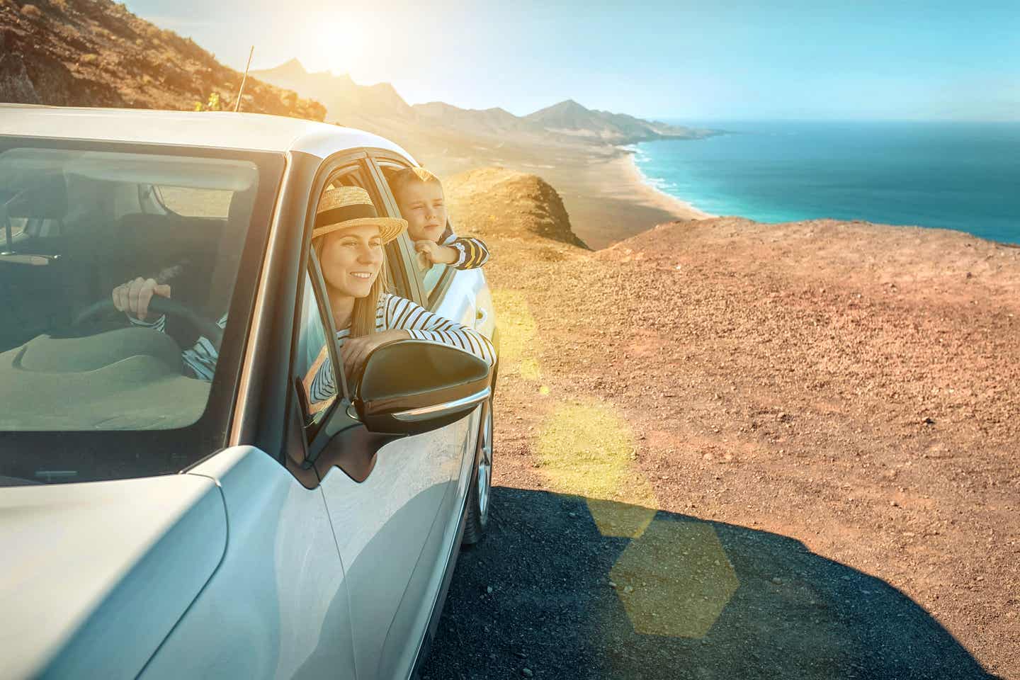 Selbstfahrer-Rundreisen. Frau mit Sohn im Auto an einem Strand.