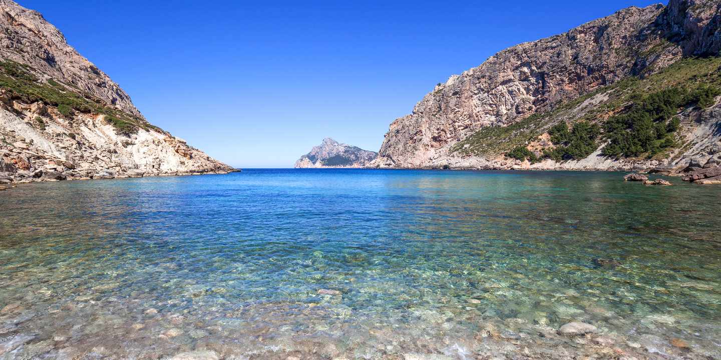 Kiesstrand der Cala Boquer auf Mallorca mit klarem Wasser und steilen Felswänden entlang der ruhigen Bucht
