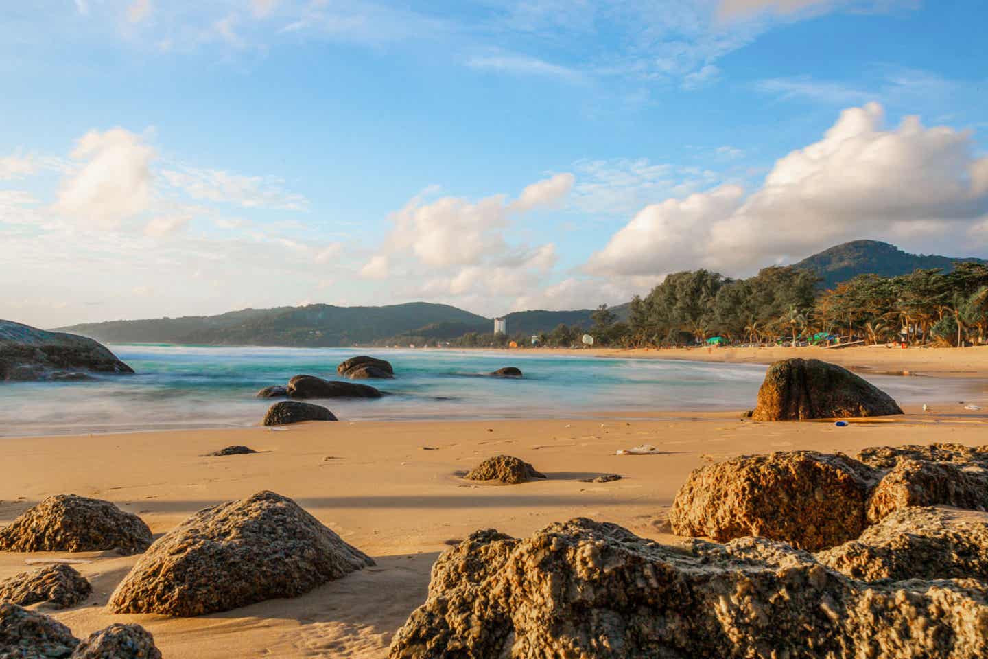 Der Kamala Beach in Phuket mit kleinen Felsen und grüner Vegetation im Hintergrund