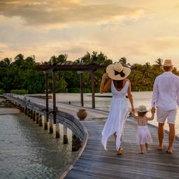 luxus-familienurlaub-eine-familie-geht-haendchenhaltend-ueber-einen-hoelzernen-pier-in-richtung-einer-tropischen-insel-g-1352015722.jpg