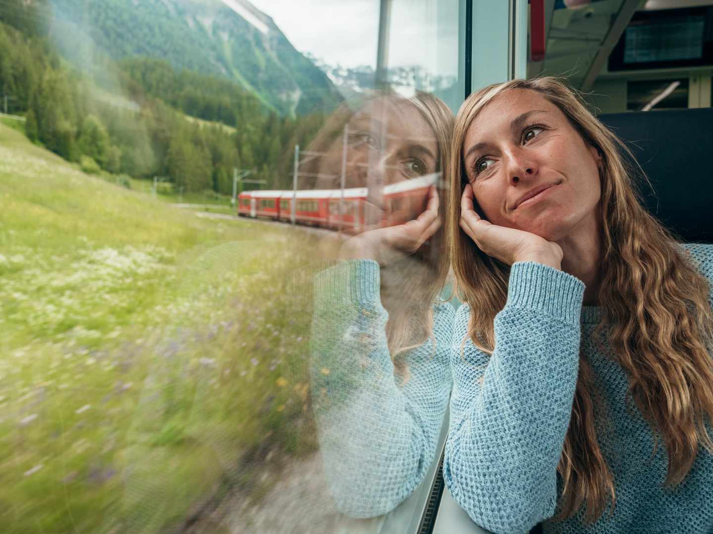 Frau schaut während einer Bahnfahrt durch die Schweiz aus dem Fenster