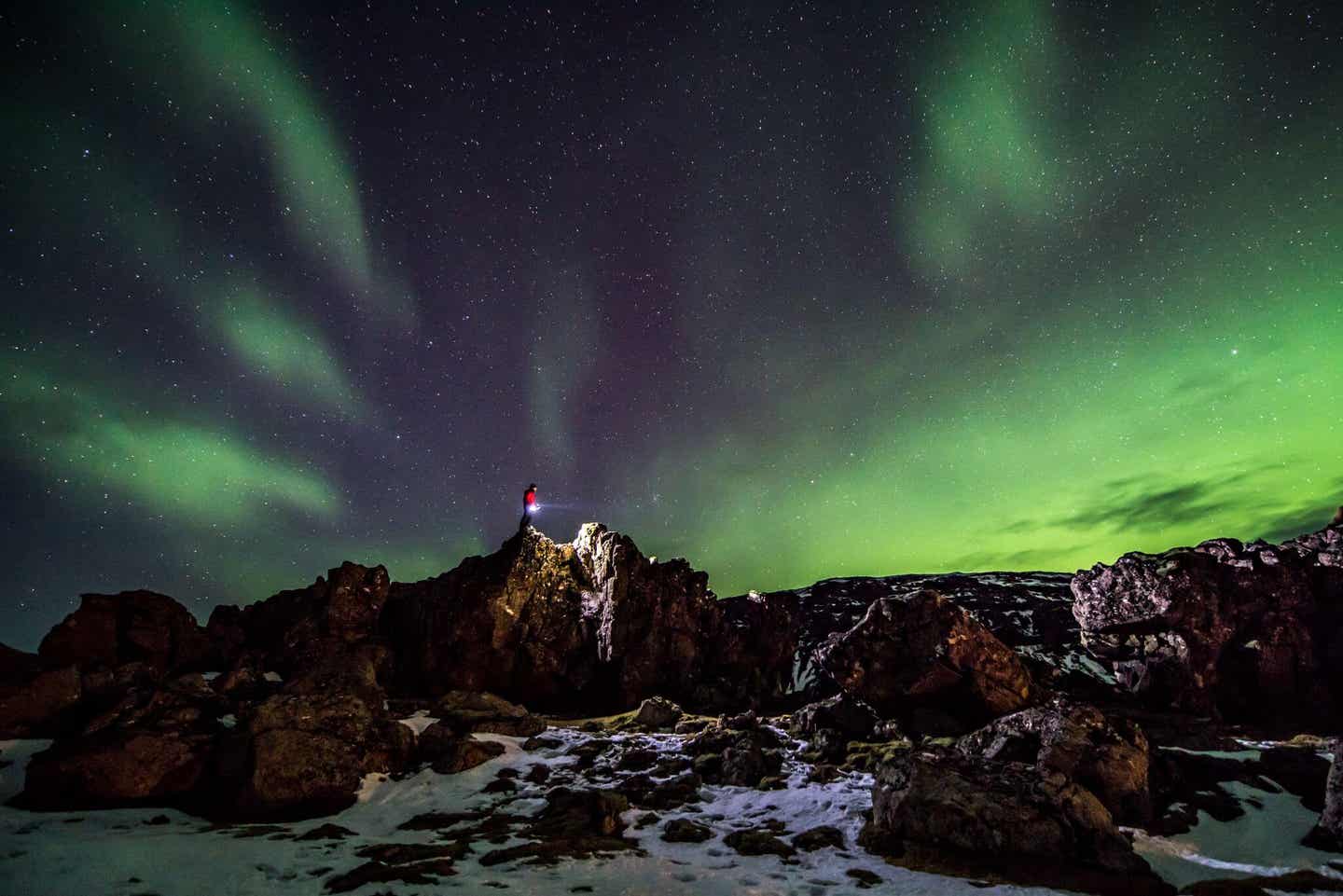 Warm angezogen, um Polarlichter zu sehen: Mann auf Felsen mit Nordlichtern