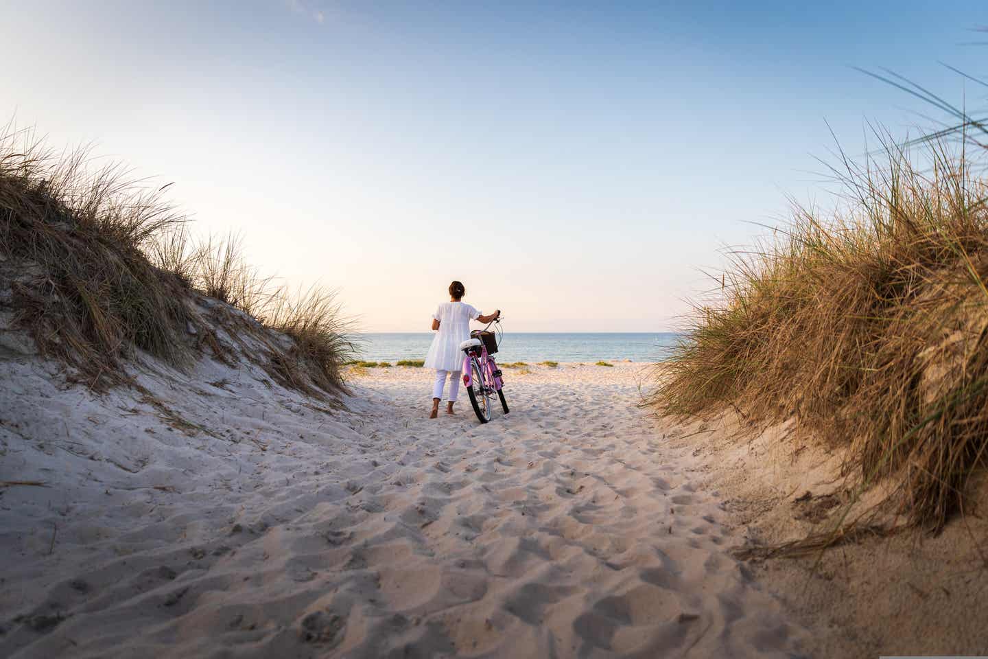 Frau mit Fahrrad zwischen Dünen am Strand von Rügen