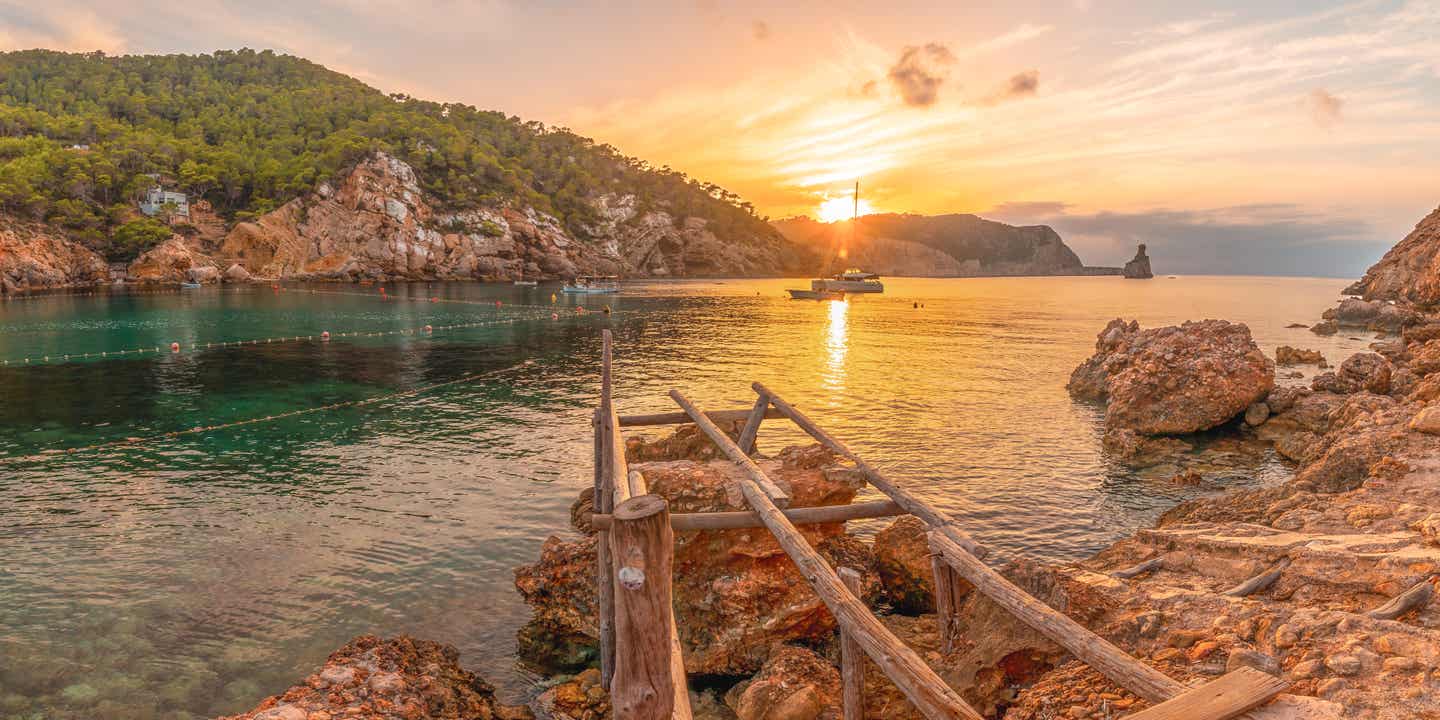 Ibizas Benirrás Strand bei Sonnenuntergang mit Blick auf Felsen, Boot und ruhige Bucht