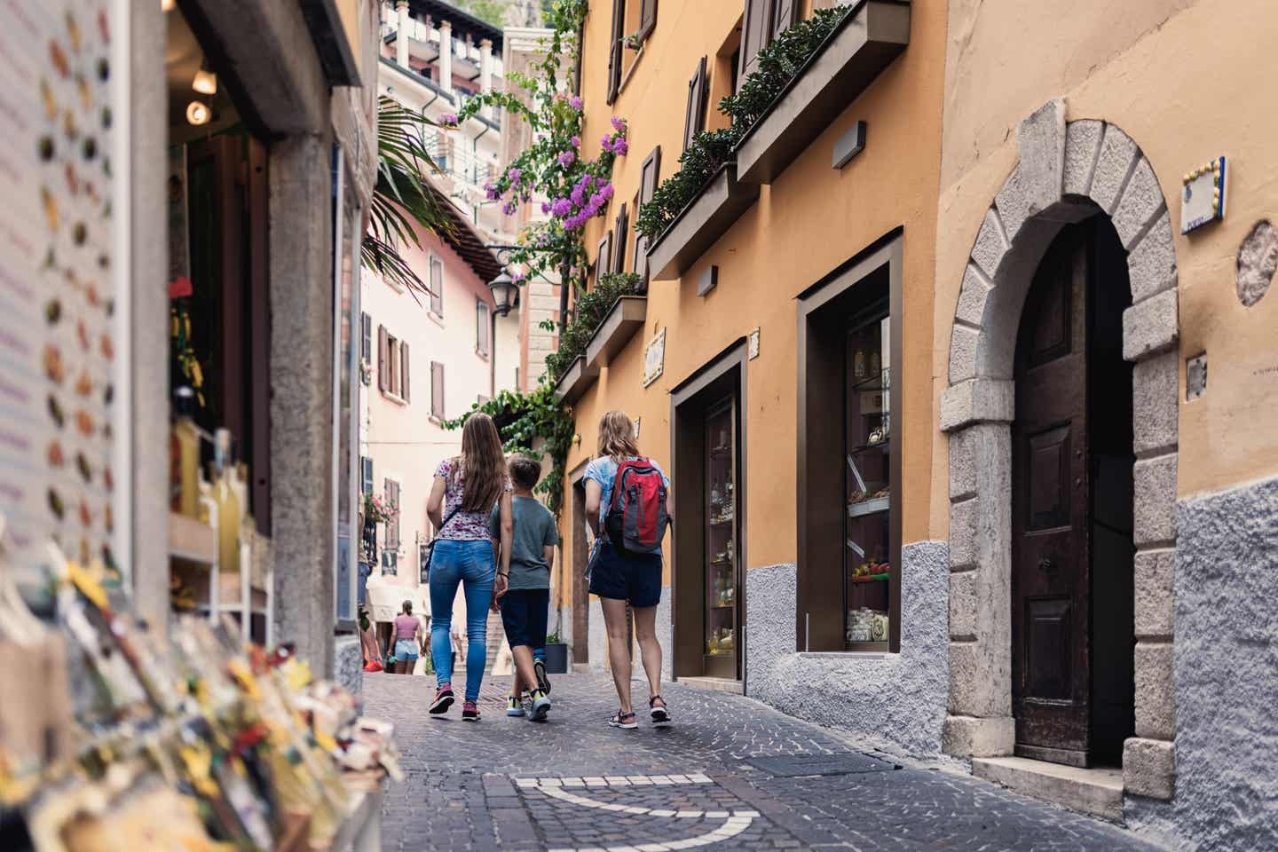 Familie spaziert durch enge Gassen mit gelben Häusern während eines Familienurlaubs am Gardasee in Limone sul Garda, Italien