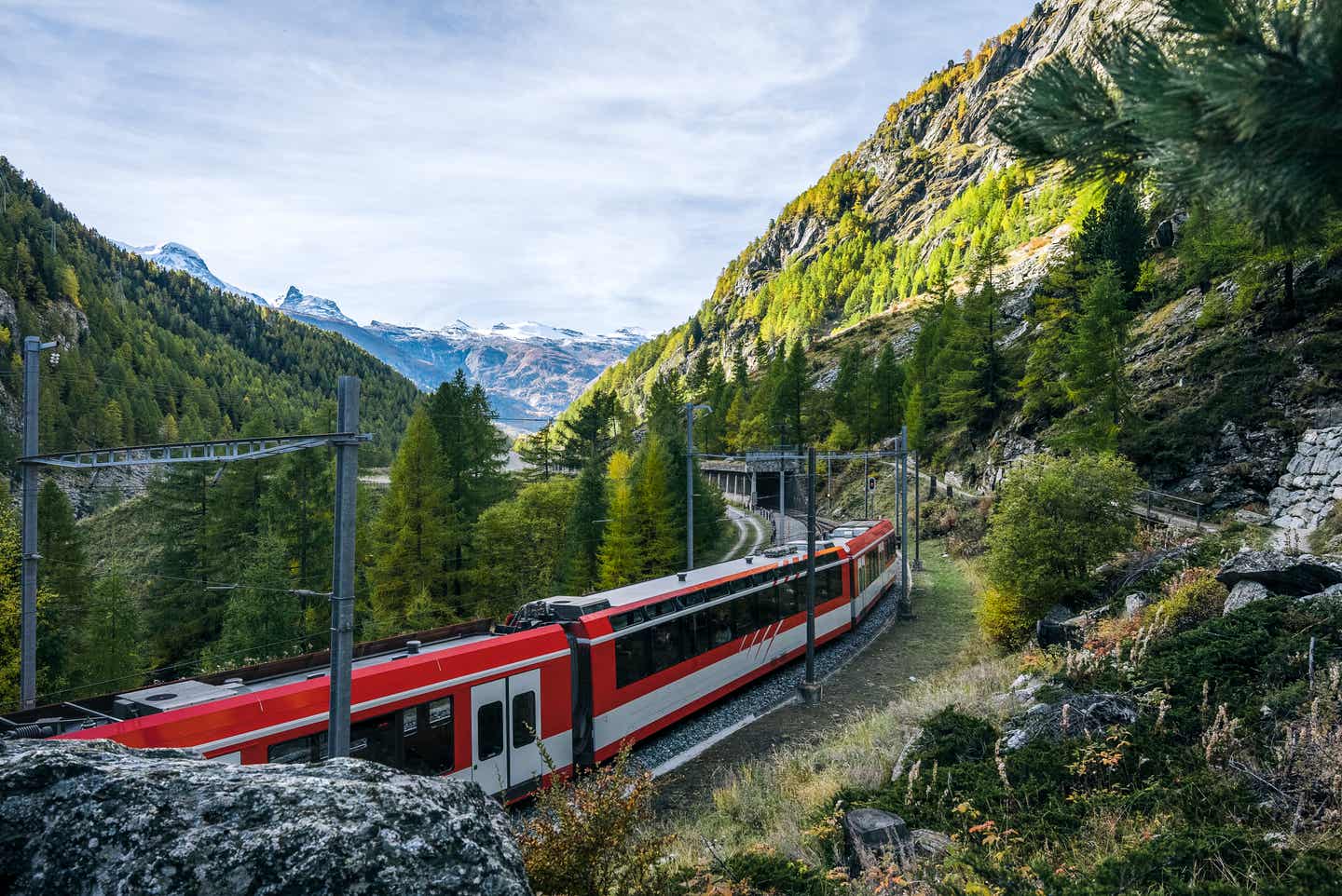 Ein nachhaltiger Fernreisezug fährt durch ein kurvenreiches Bergpanorama auf einen Tunnel zu