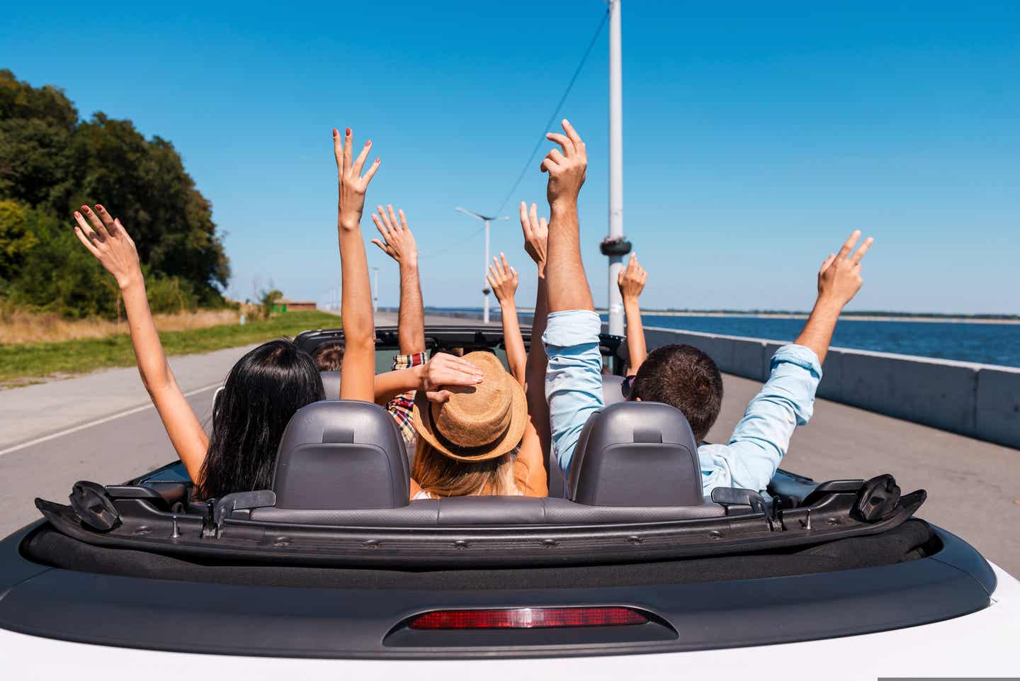 Selbstfahrer-Rundreisen: Gruppe sitzt in einem Cabrio und streckt die Hände in einigen blauen, sonnigen Himmel.