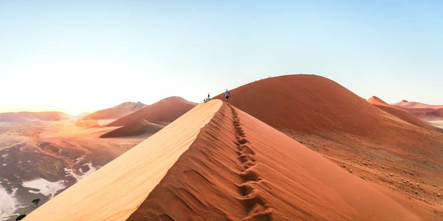 Menschen wandern auf dem Grat einer hohen Sanddüne bei Sonnenaufgang in einer Wüstenlandschaft