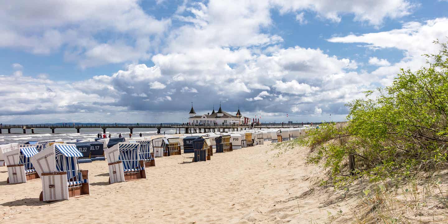 Strandkörbe am Sandstrand von Ahlbeck auf Usedom, mit Blick auf die historische Seebrücke und die Ostsee unter bewölktem Himmel