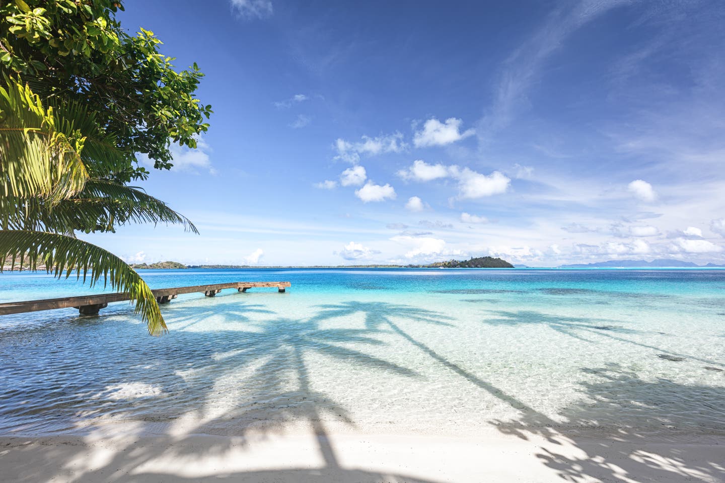 Glasklares Wasser an hellem Strand mit Holzsteg auf Bora Bora