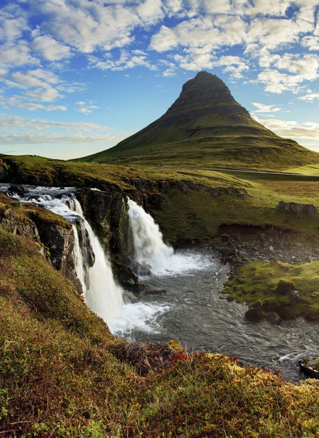 Island Rundreisen Island Wasserfall und Berg im Hintergrund bei Sonnenschein