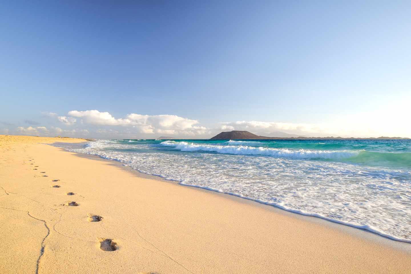 Blick über den Strand Grandes Playas de Corralejo auf Fuerteventura mit Fußspuren im Sand und den Inseln Lobos und Lanzarote