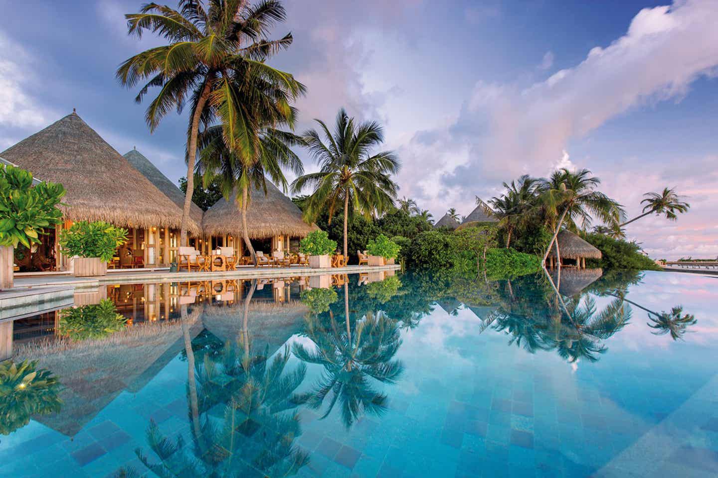 Pool, in dem sich Palmen spiegeln, mit Bungalows im Milaidhoo Island Maledives