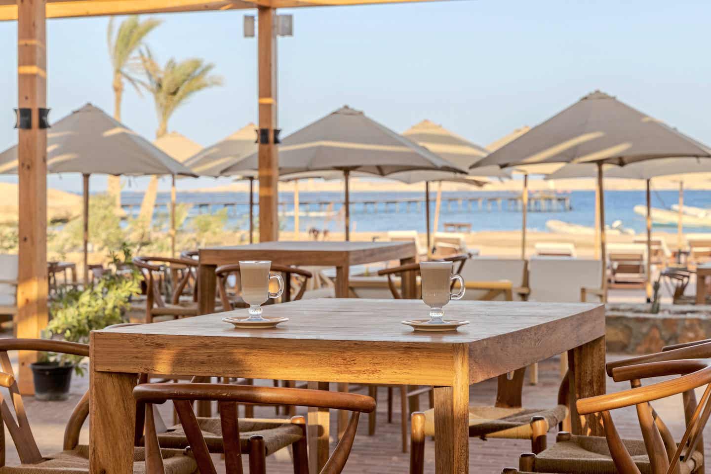 Außenterrasse des Aldiana Clubhotel Naga Bay mit Palmen, Sonnenschirmen und Gästen beim Essen in entspannter Urlaubsatmosphäre