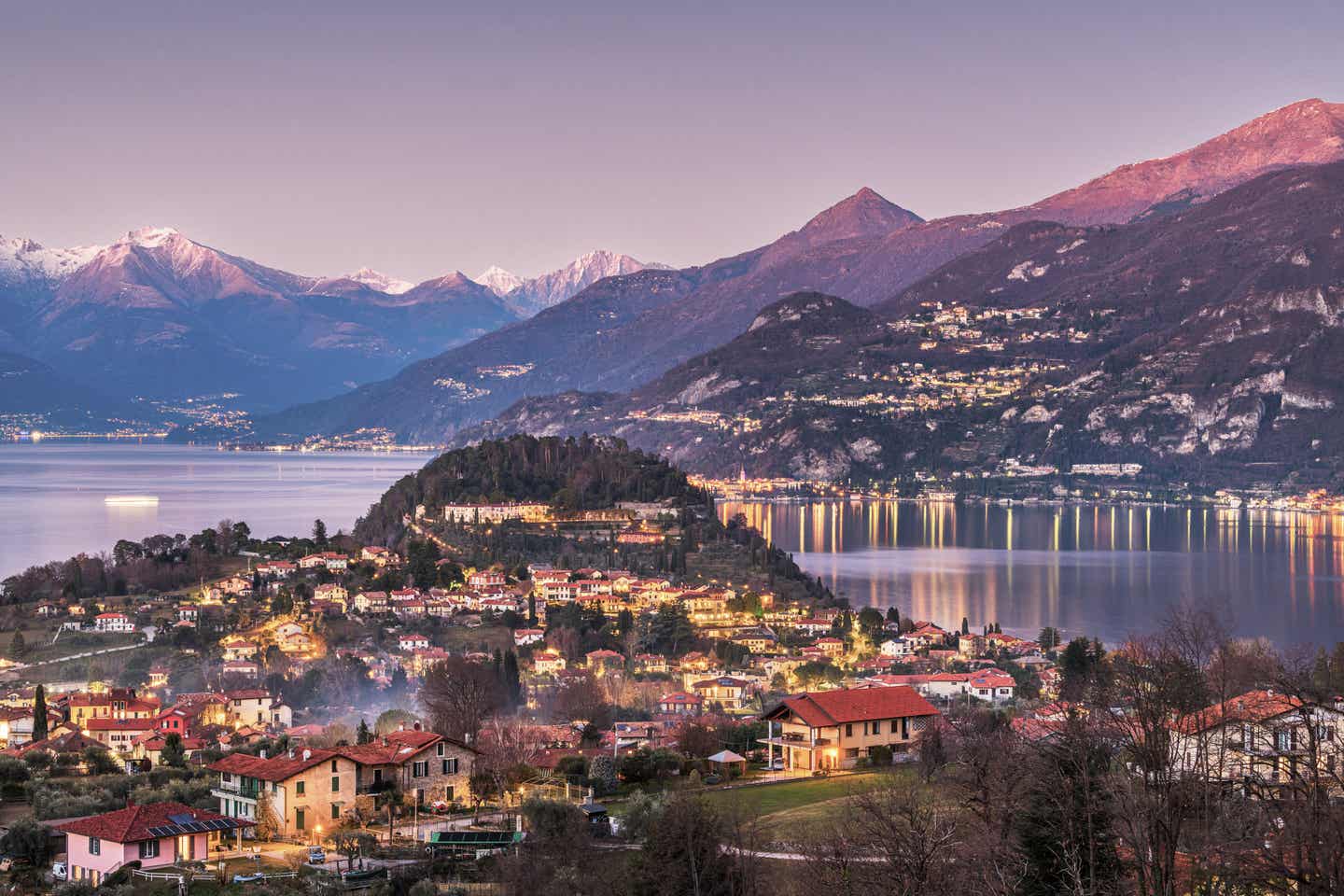 Comer See Urlaub mit DERTOUR. Panoramaaufnahme von Bellagio und Como in der Abenddämmerung mit Alpen im Hintergrund