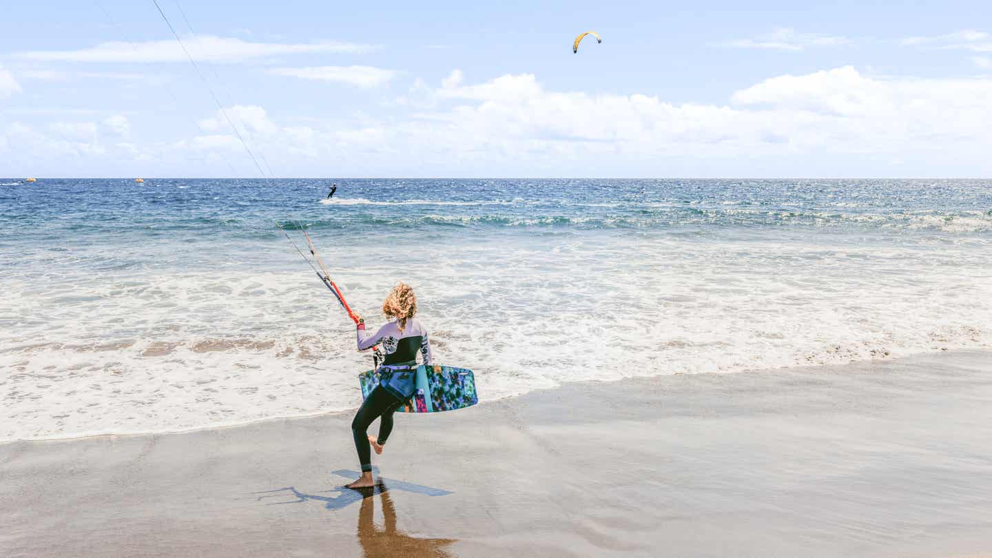 Frau mit Kiteboard läuft am Strand von Tarifa ins Wasser – bereit zum Surfen bei guten Windbedingungen 