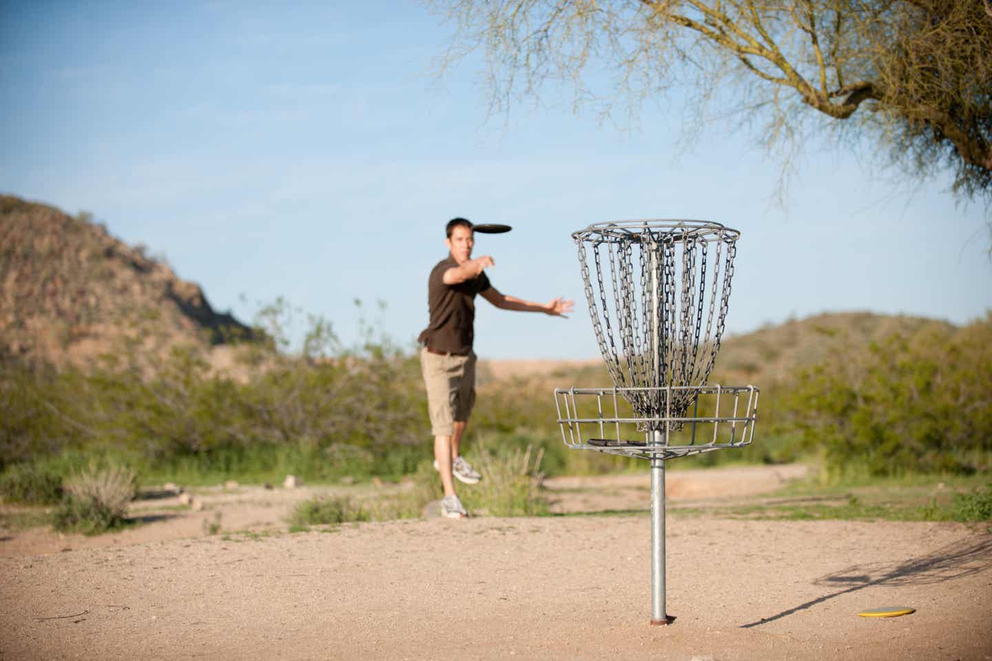 Mann wirft auf einem Parcours mit einem Frisbee auf einen Korb aus Stahlketten