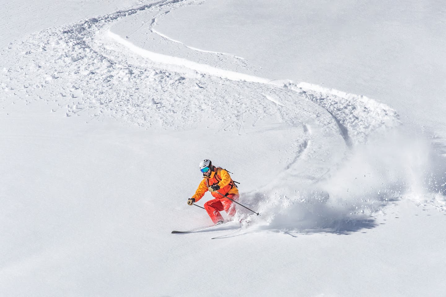 Ein Skifahrer in orangefarbener Jacke und Hose fährt ein S in den Tiefschnee auf einer Skipiste in Kanada