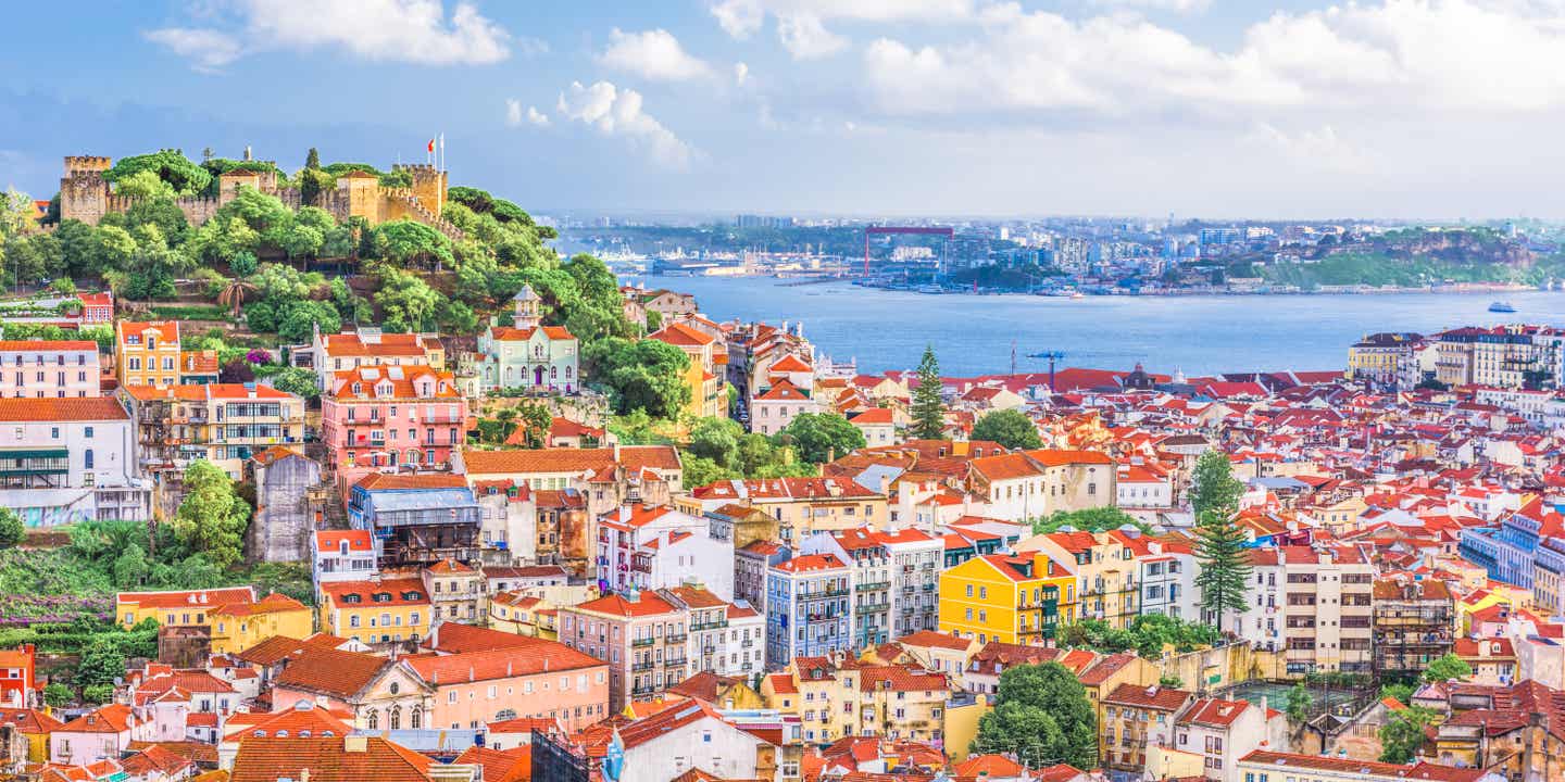 Blick auf Lissabon mit bunten Häusern, dem Castelo de Sao Jorge und dem Tejo im Hintergrund