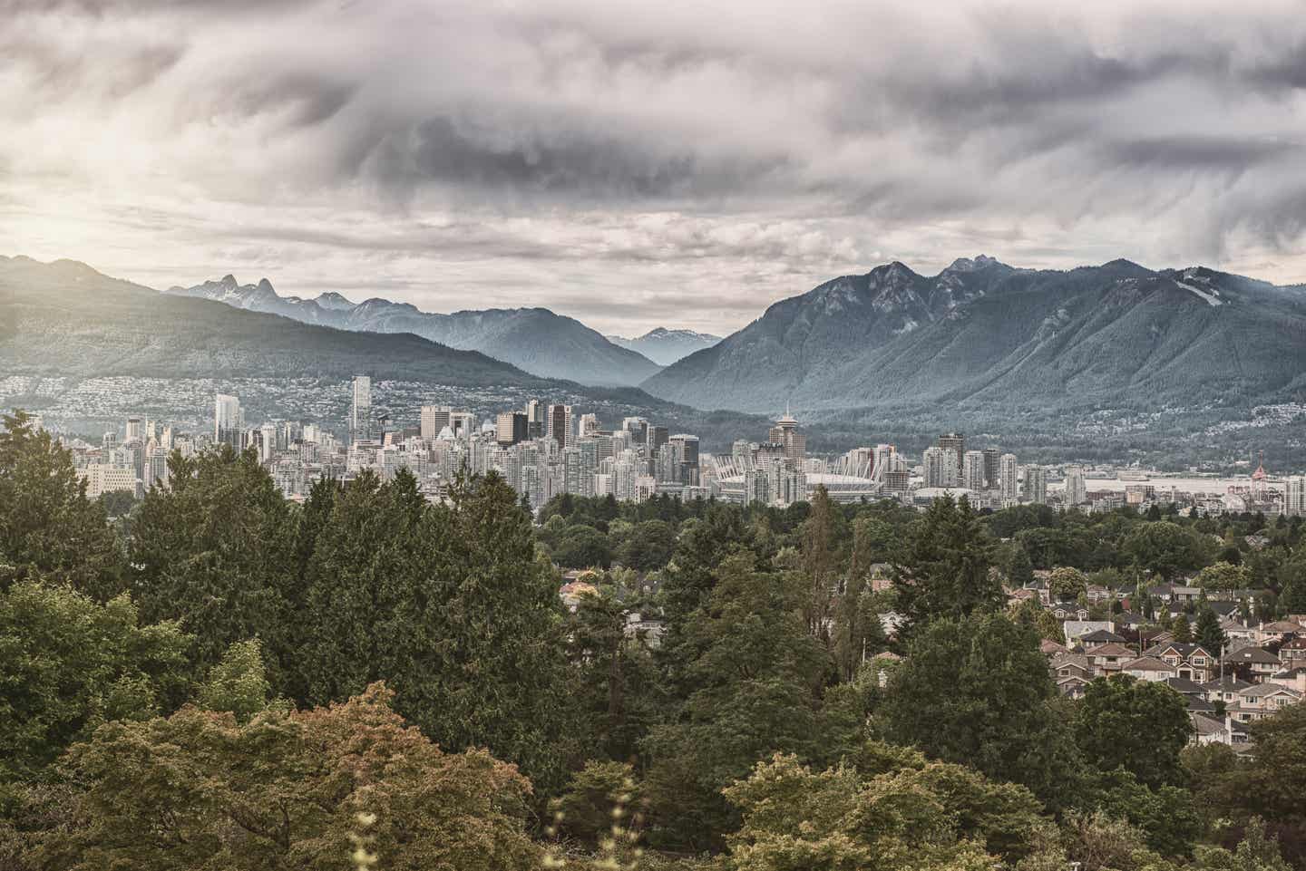 Vancouver Urlaub mit DERTOUR. Vancouvers Skyline aus der Ferne mit Wald vorn und Bergen im Hintergrund