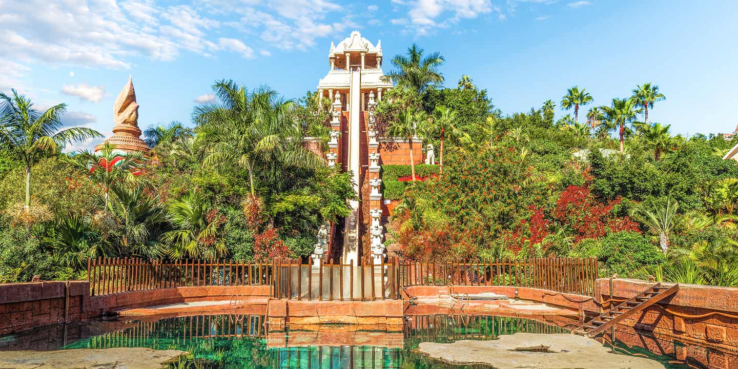 Hohe Wasserrutsche „Tower of Power“ im Siam Park auf Teneriffa, umringt von tropischen Bäumen und Palmen mit Wasserbecken im Vordergrund 