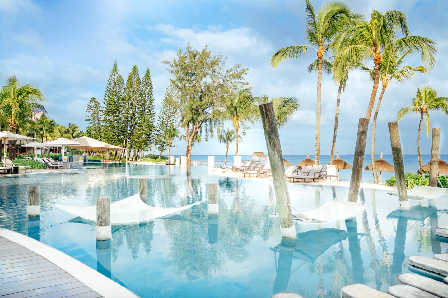 Pool mit Sonnenliegen und Relaxschaukeln im Wasser direkt am Strand