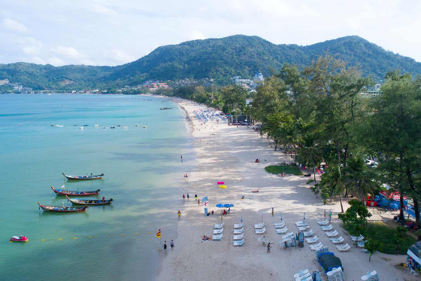 Blick auf den Patong Strand in Phuket mit Sonnenliegen und Holzbooten