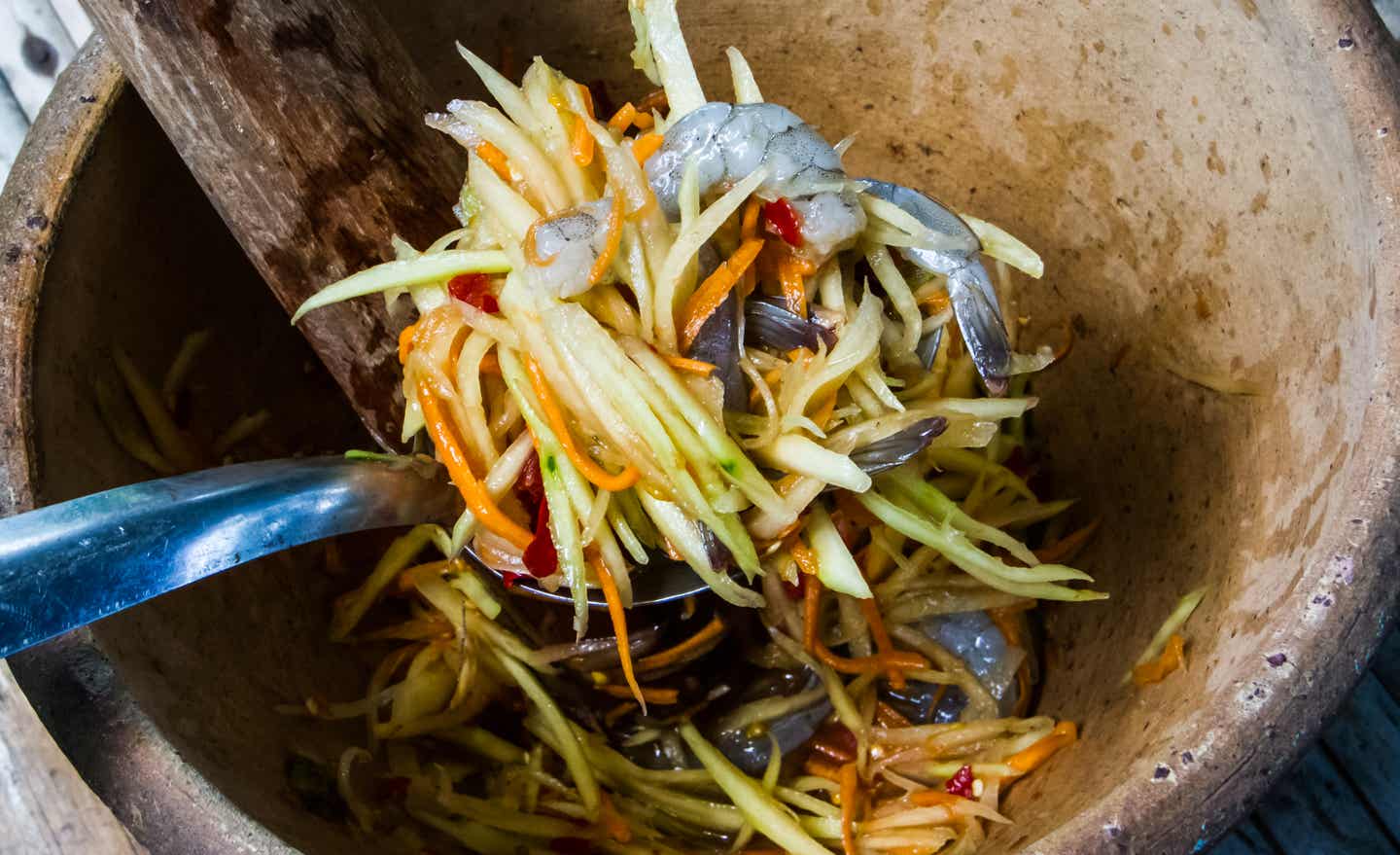 Schüssel aus Steingut gefüllt mit geraspeltem Gemüse und rohen Garnelen, darunter eine silberfarbene Kelle