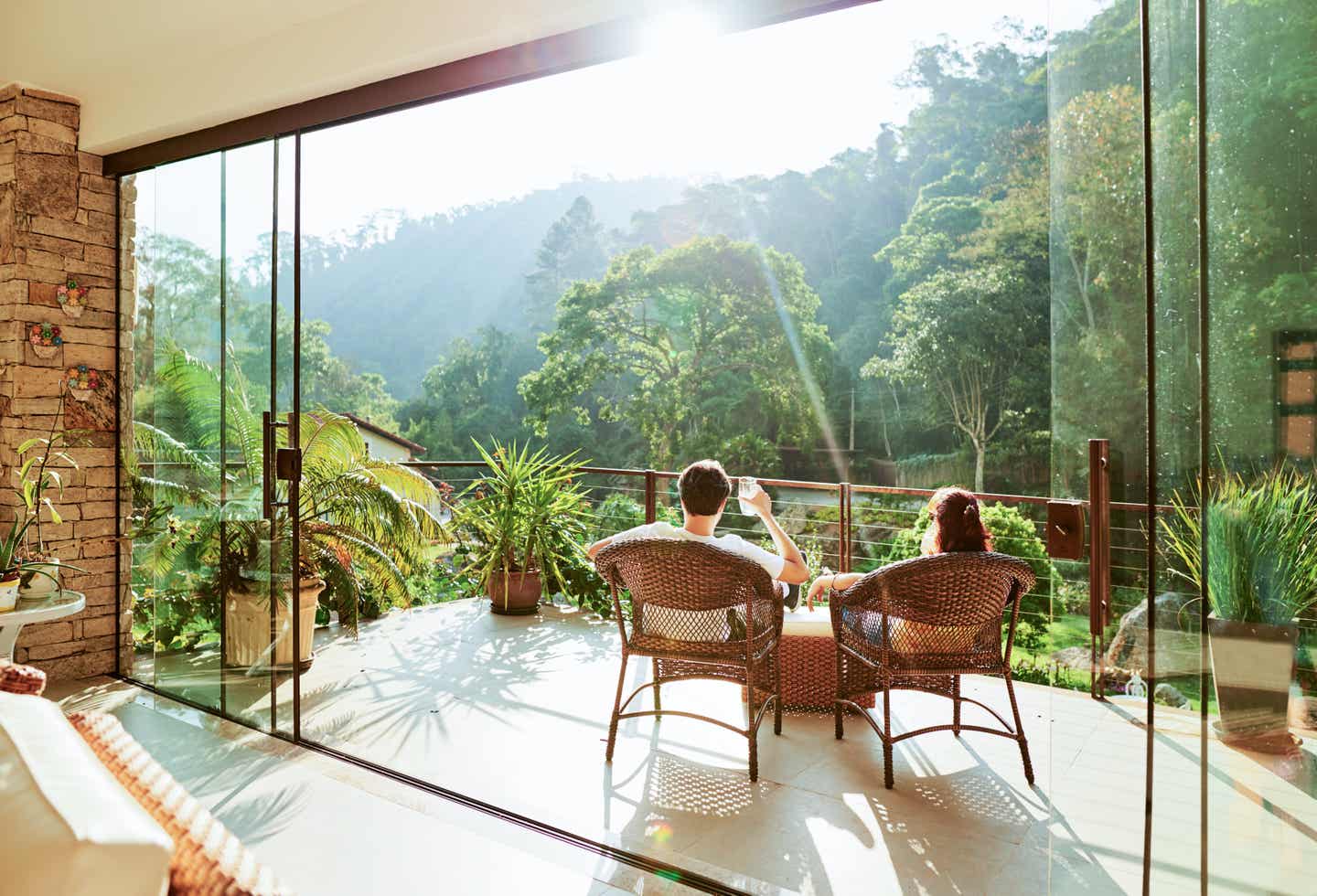 Ein Paar sitzt auf einem offenen Balkon seines Hotelzimmers und blickt in den üppigen grünen Wald