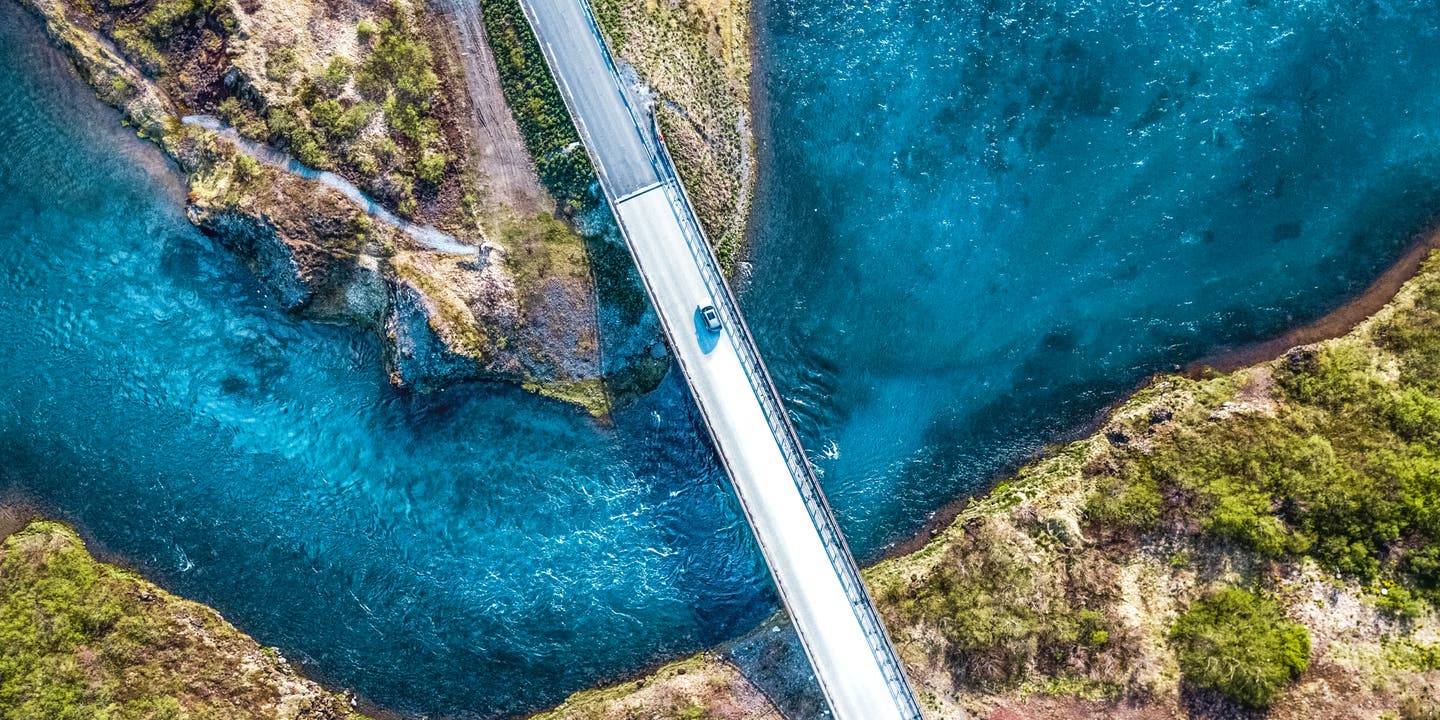 Vogelperspektive auf ein Auto auf einer Brücke auf dem Golden Circle in Island über blauem Wasser