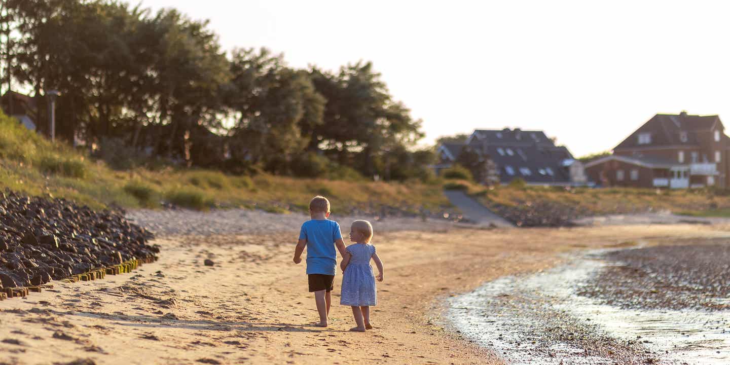 Zwei Kinder spazieren barfuß am Strand der Nordseeinsel Amrum entlang, im goldenen Licht der Abendsonne