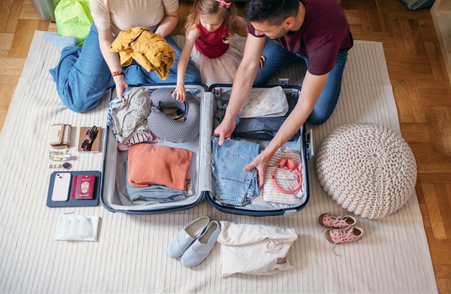 Eine junge Familie sitzt gemeinsam auf dem Boden und packt sorgfältig ihren Koffer für den bevorstehenden Inselurlaub mit Kindern