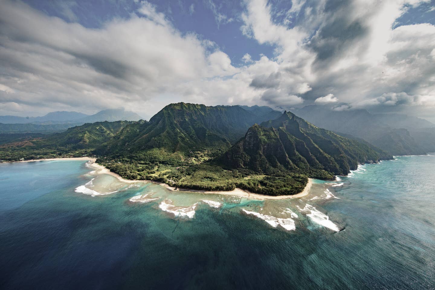 Kauai Urlaub mit DERTOUR. Luftaufnahme der Na-Pali-Küste auf Kauai mit Strand und bergigem Urwald dahinter