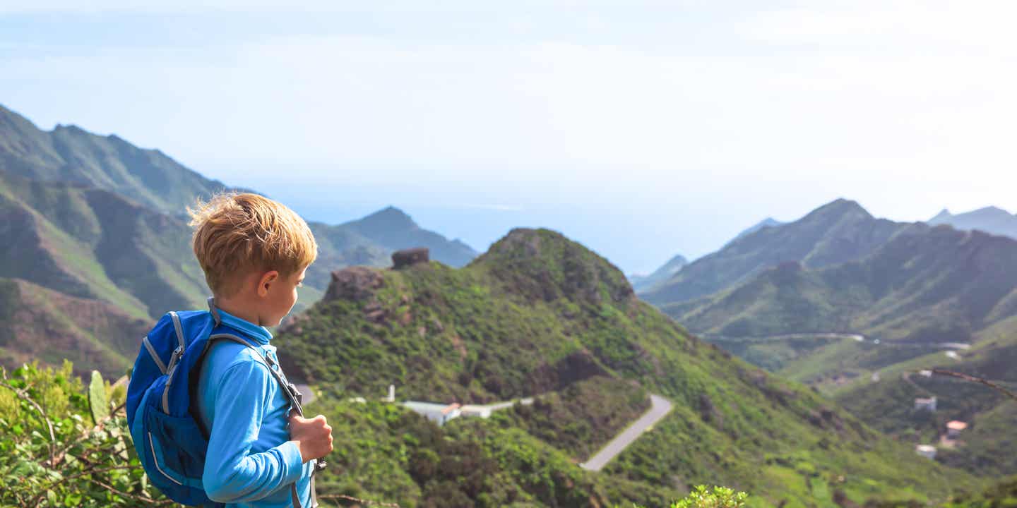 Kleiner Junge mit Rucksack genießt beim Inselurlaub mit der Familie das Wandern in den grünen Bergen von Teneriffa